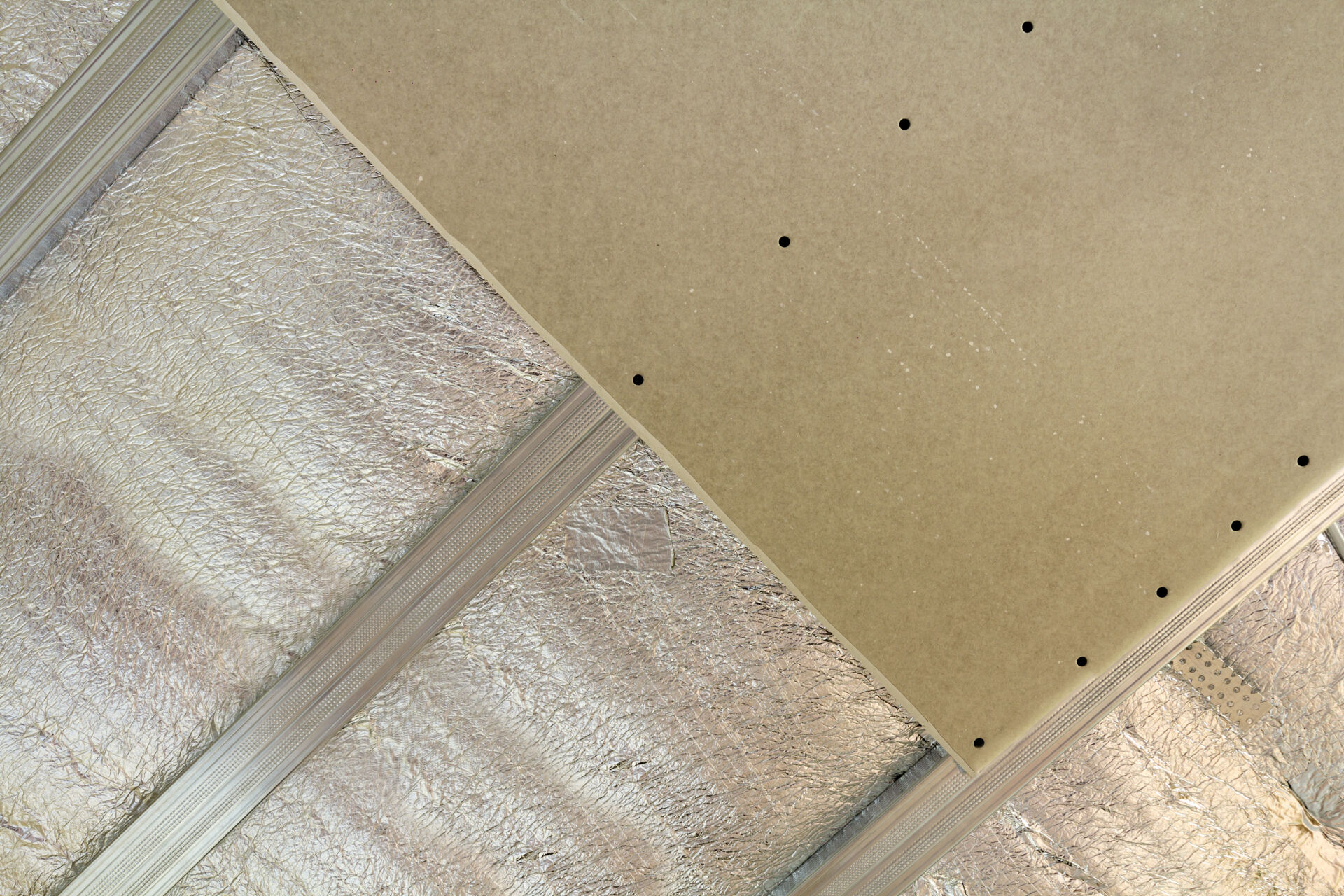 Close-up bottom view of unfinished room under construction and renovation with silver aluminum insulation foil and drywall on walls and ceiling. Professional work and renovation concept.